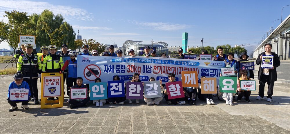 야외에서 경찰과 사람들이 안전 홍보 배너를 들고 모여서 사진을 찍고 있다