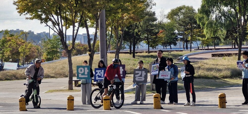 야외에서 자전거 탄 사람이 안전 팻말을 든 사람들과 함께 서 있는 장면