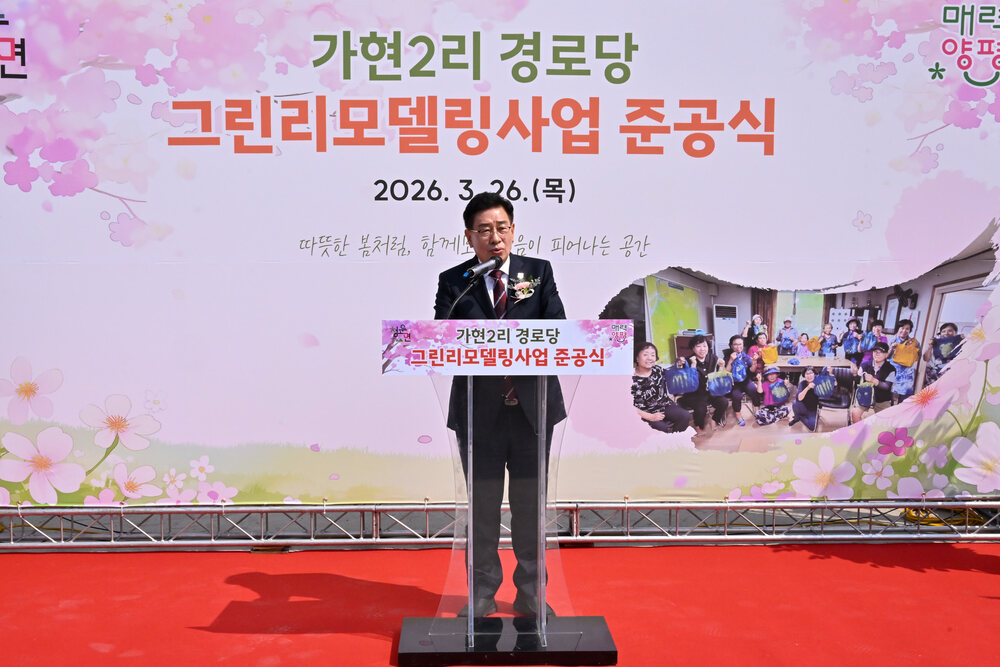빨간 카펫 위에 서서 연단에서 연설하는 남성과 뒤에 행사 배너가 보임
