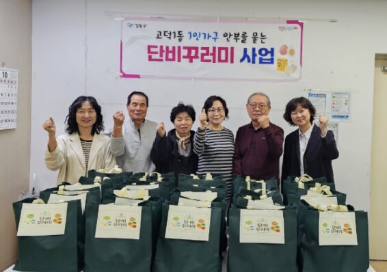 벽에 걸린 현수막 아래 선물 꾸러미 앞에 서 있는 여섯 명의 사람들이 주먹을 들어 응원하는 모습이다.