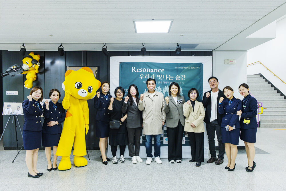 전시장 입구에서 캐릭터 탈을 쓴 인물과 여러 사람이 단체 사진을 찍는 모습