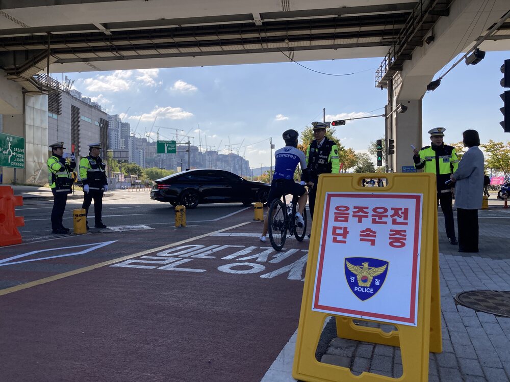 자전거 탄 사람과 경찰들이 도로변에서 음주운전 단속 안내판 옆에 서 있다
