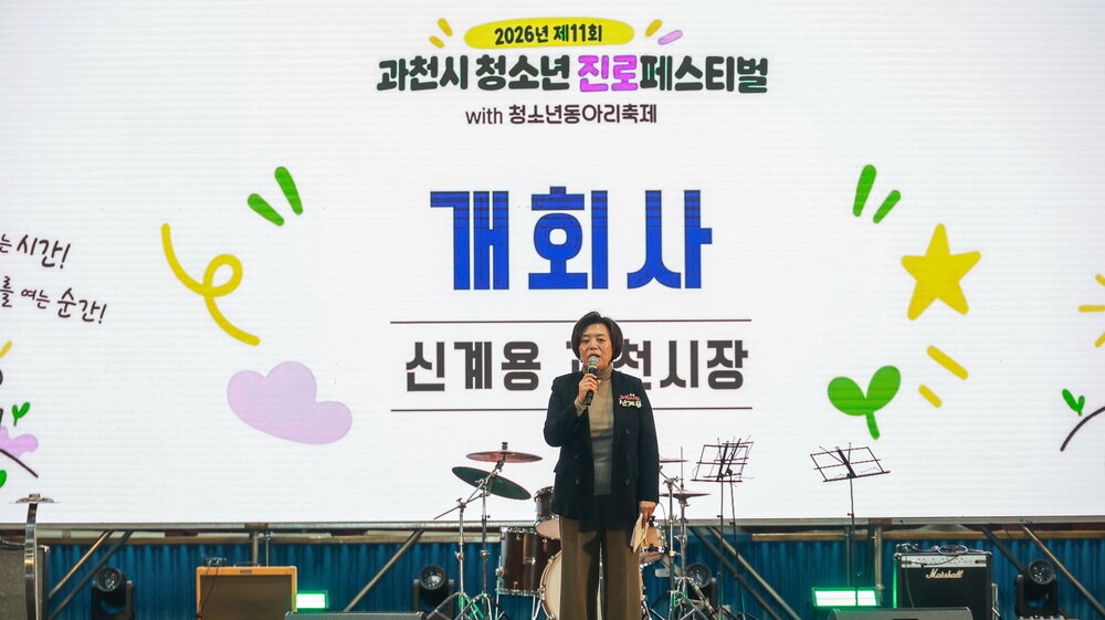 개회사 배경 화면이 있는 무대 위에서 마이크를 들고 말하는 인물 모습